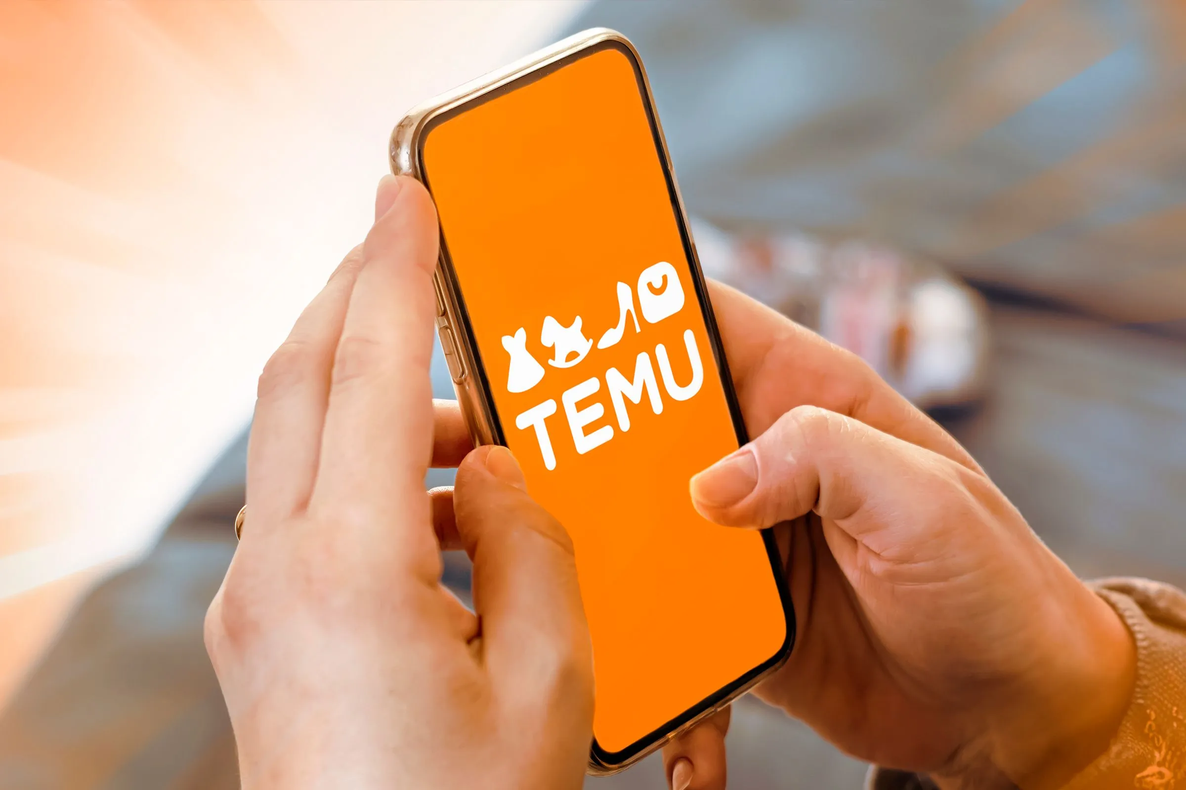 Bàn tay đang cầm điện thoại thông minh hiển thị logo ứng dụng Temu trên màn hình, tượng trưng cho trải nghiệm sử dụng app Temu.