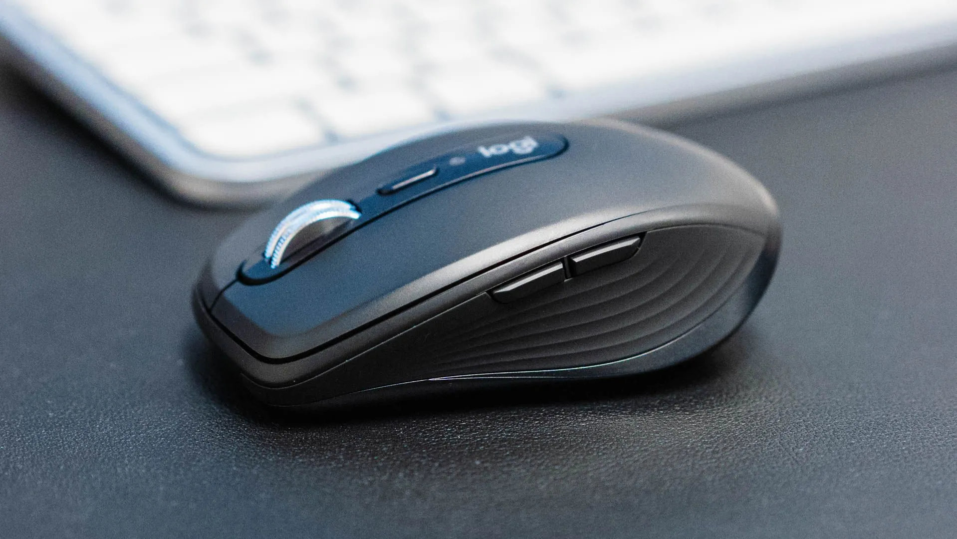 Góc nhìn nghiêng của chuột Logitech MX Anywhere 3S đặt trước bàn phím trên bàn làm việc.