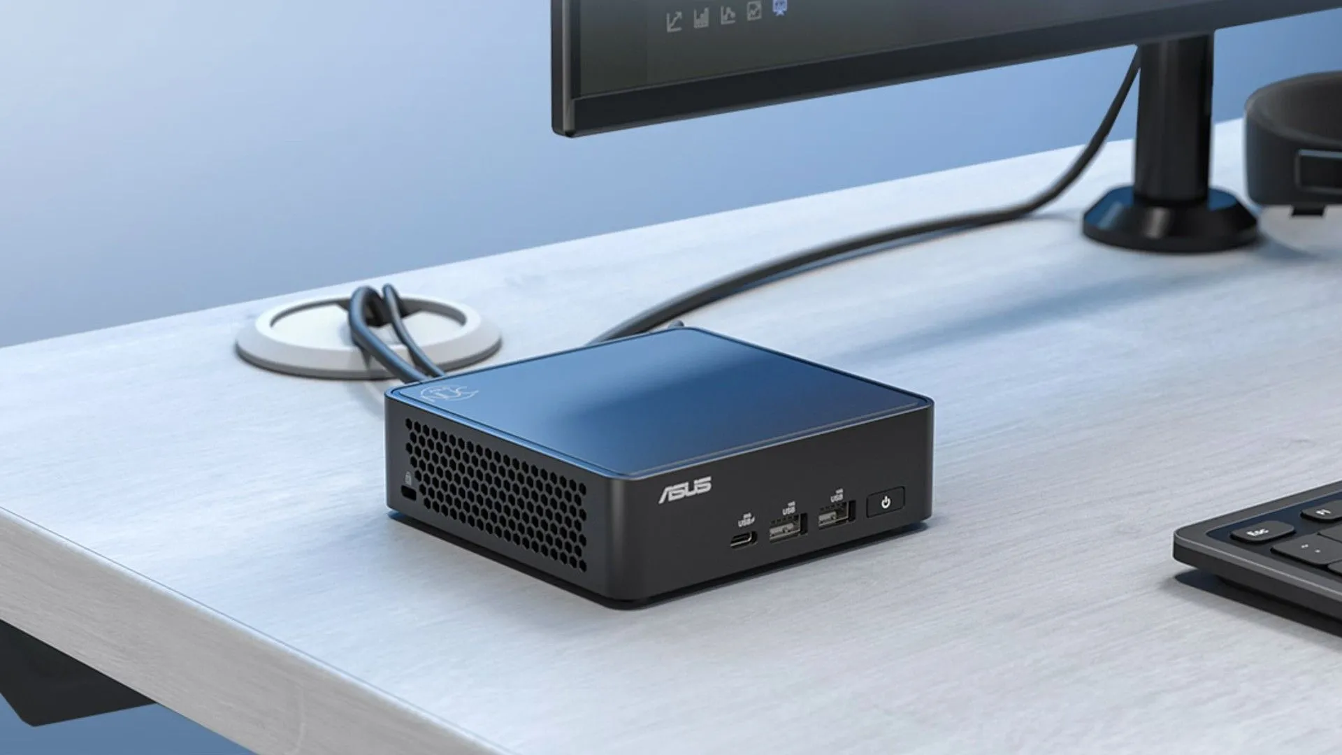 Máy tính mini ASUS NUC 15 Pro màu đen được kết nối với màn hình và các thiết bị ngoại vi, đặt trên bàn làm việc