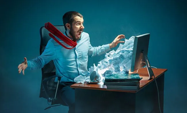 Một người đàn ông tỏ ra khó chịu khi nhận email spam và lừa đảo trên màn hình máy tính.