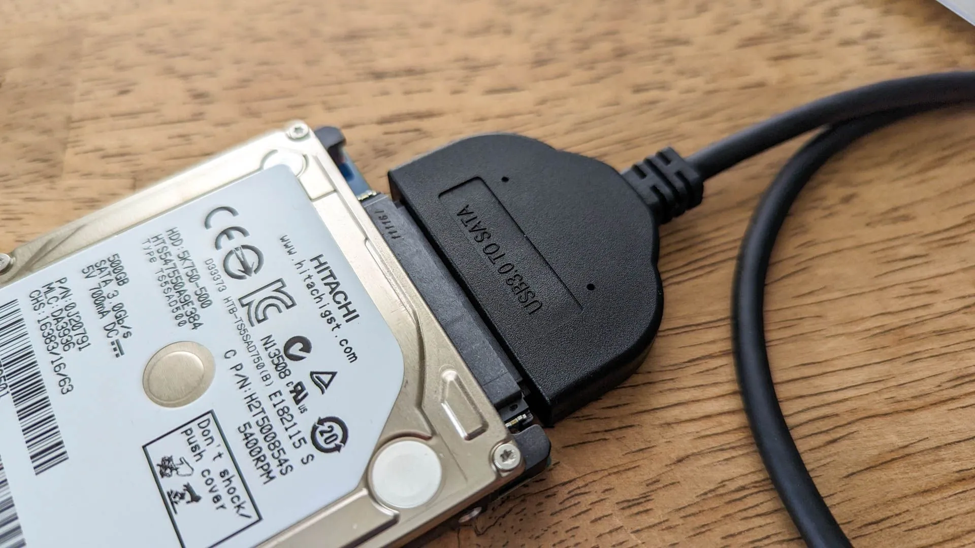 Ổ đĩa cứng kết nối với bộ chuyển đổi USB trên bề mặt gỗ, minh họa cho việc kiểm tra dung lượng sử dụng với lệnh du.
