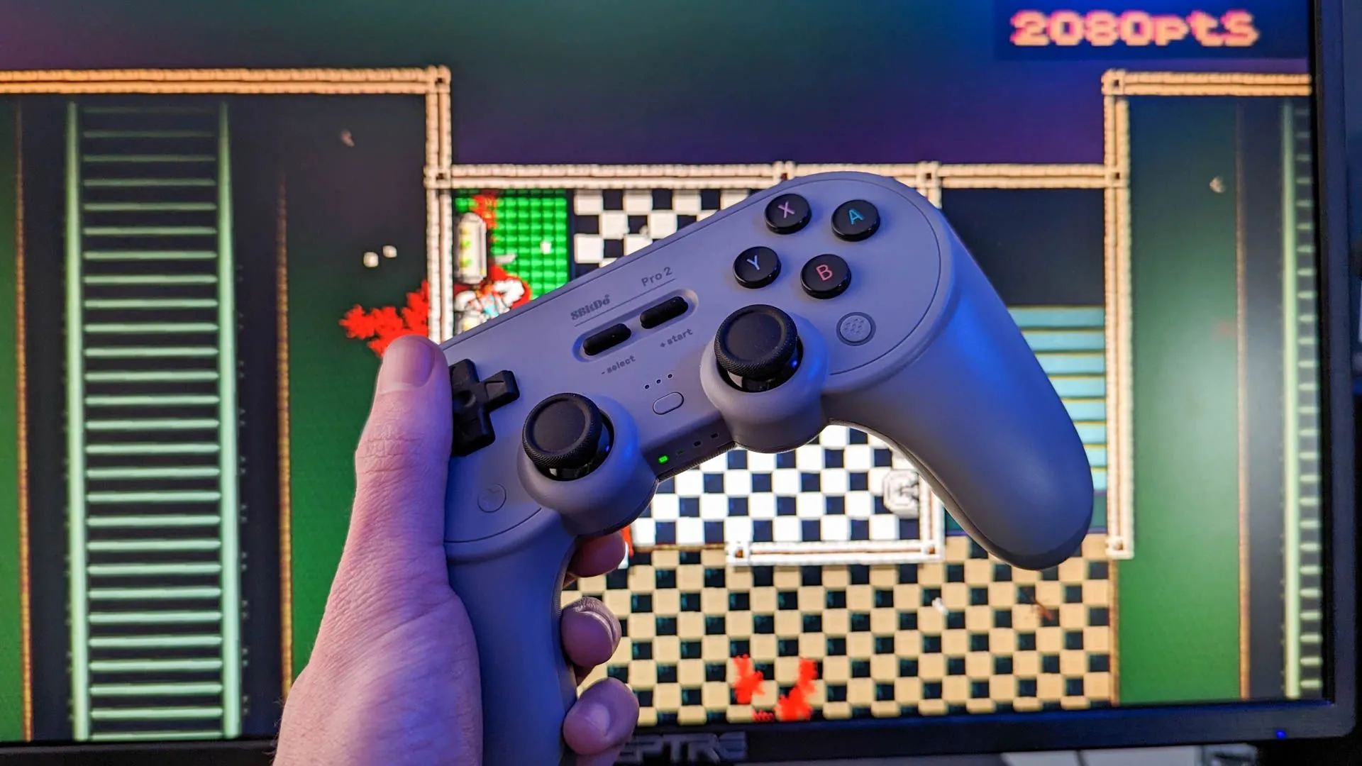 Tay cầm chơi game không dây 8Bitdo Pro 2 kết nối với màn hình máy tính, minh họa trải nghiệm gaming hiện tại trên hệ điều hành Linux.