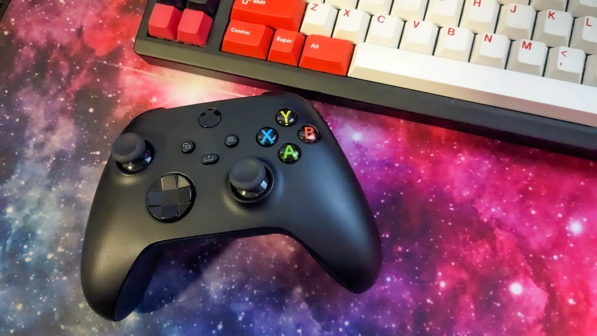 Tay cầm Xbox đặt cạnh bàn phím cơ và chuột trên thảm lót chuột chuyên game.