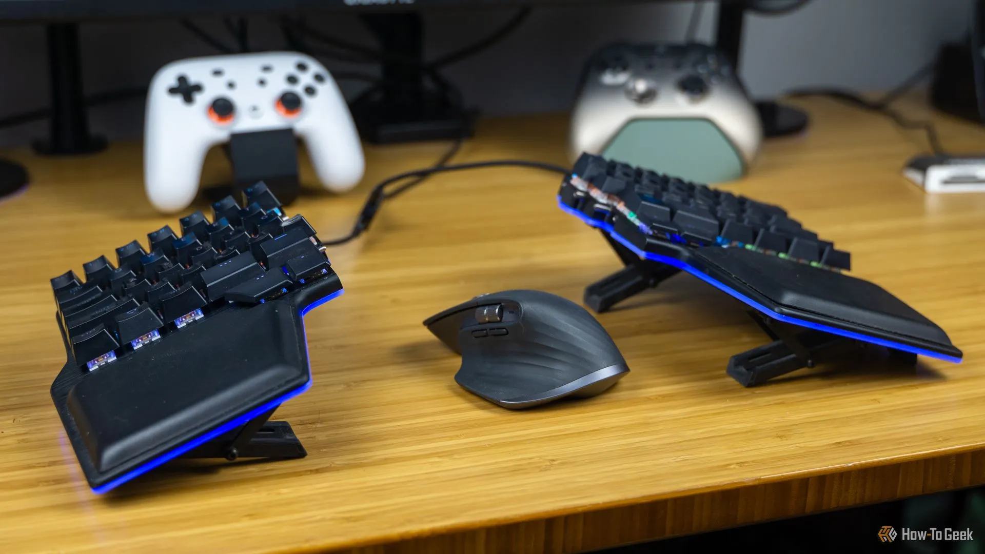 Bàn phím cơ Dygma Raise và chuột MX Master 3 trên bàn tre, cùng các bộ điều khiển chơi game, gợi ý về sự thoải mái trong thiết lập chơi game.