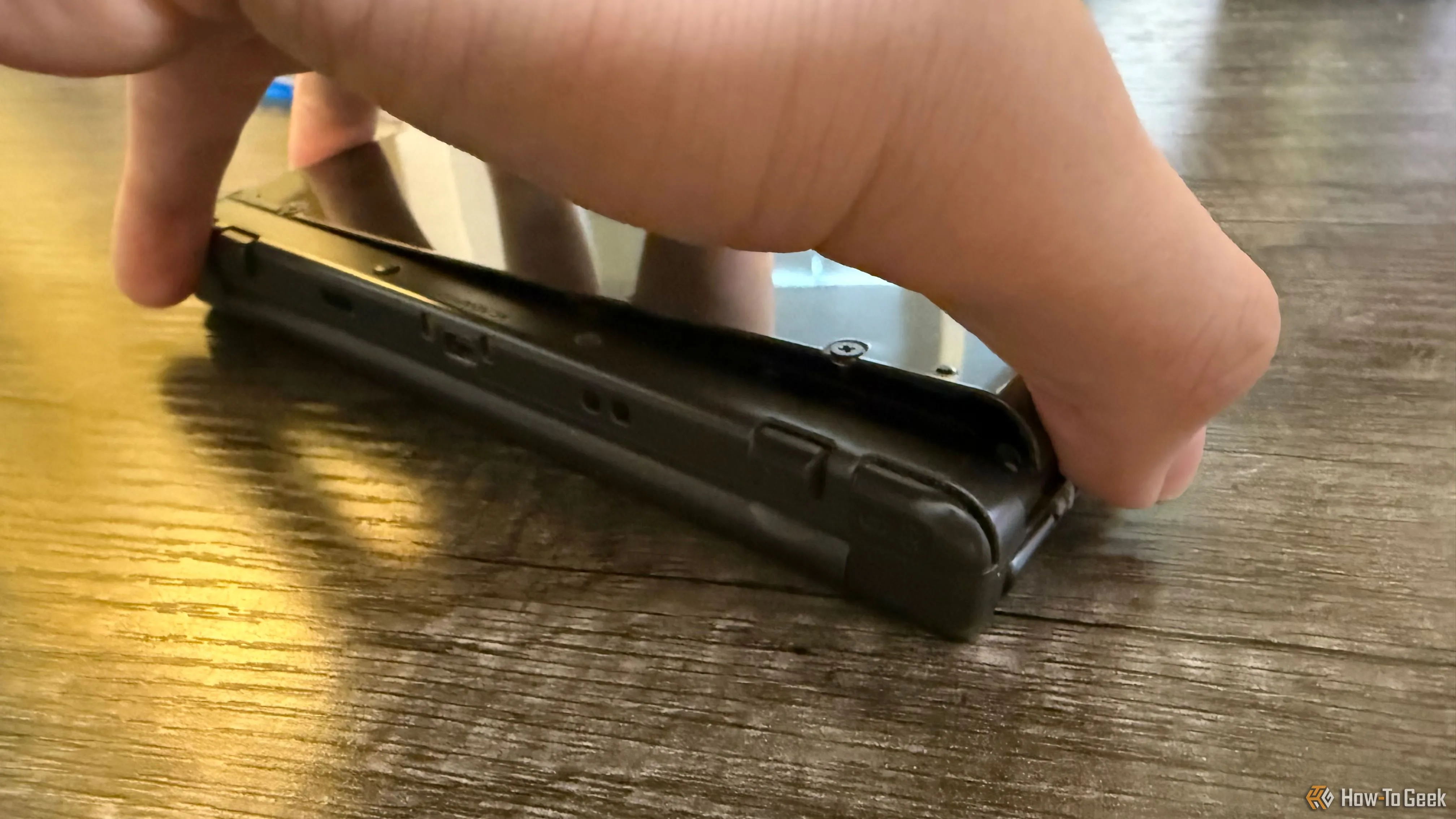 Bàn tay đang nhẹ nhàng tháo nắp lưng của máy chơi game New Nintendo 3DS XL, để lộ khoang chứa pin.