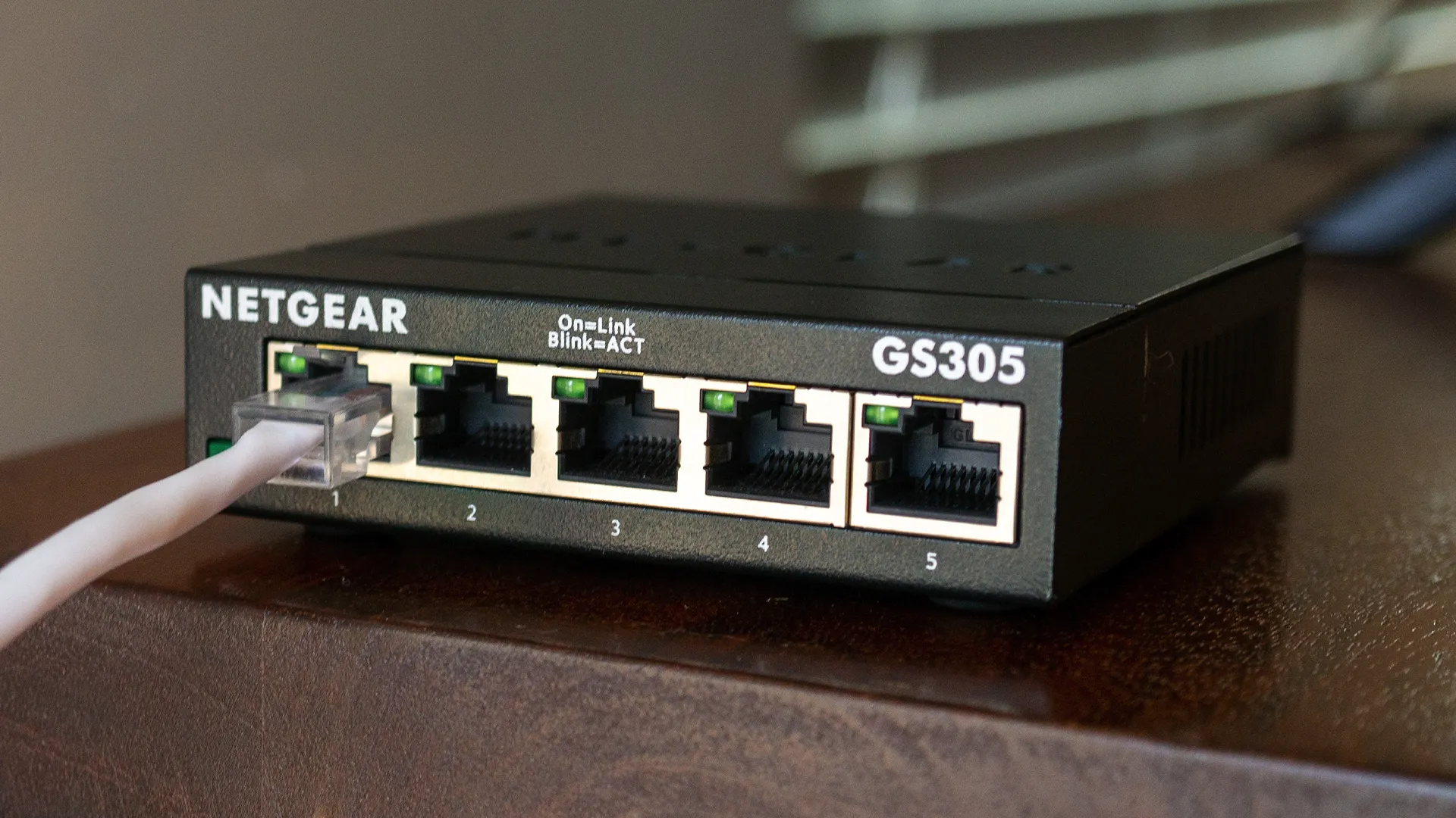 Bộ chia mạng Netgear tốc độ Gigabit với một cáp Ethernet đang kết nối, minh họa khả năng truyền dữ liệu nhanh chóng của switch giá rẻ.