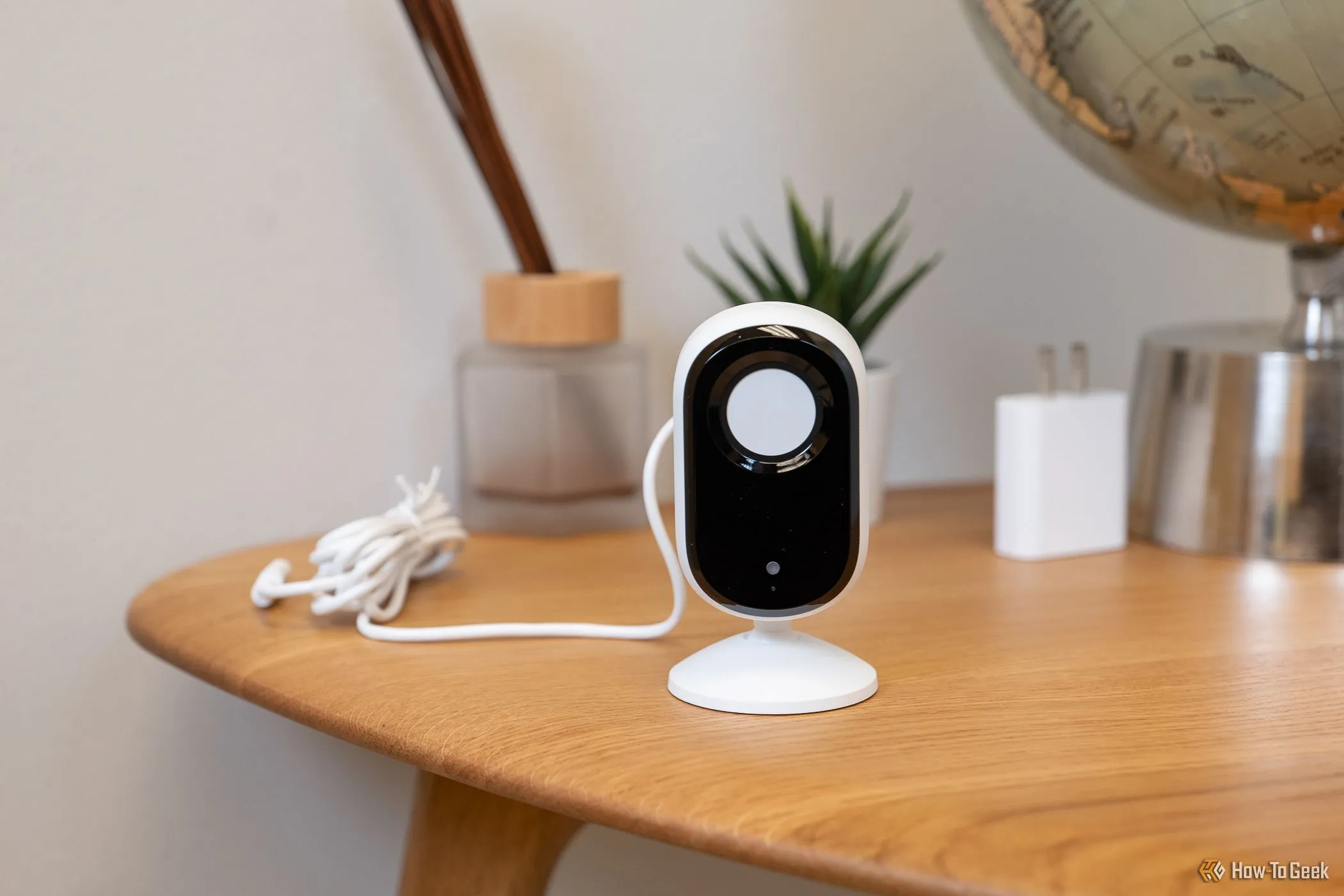 Camera an ninh Arlo Essential Indoor Cam (2K) với màn che riêng tư đang đóng, đặt trên bàn.