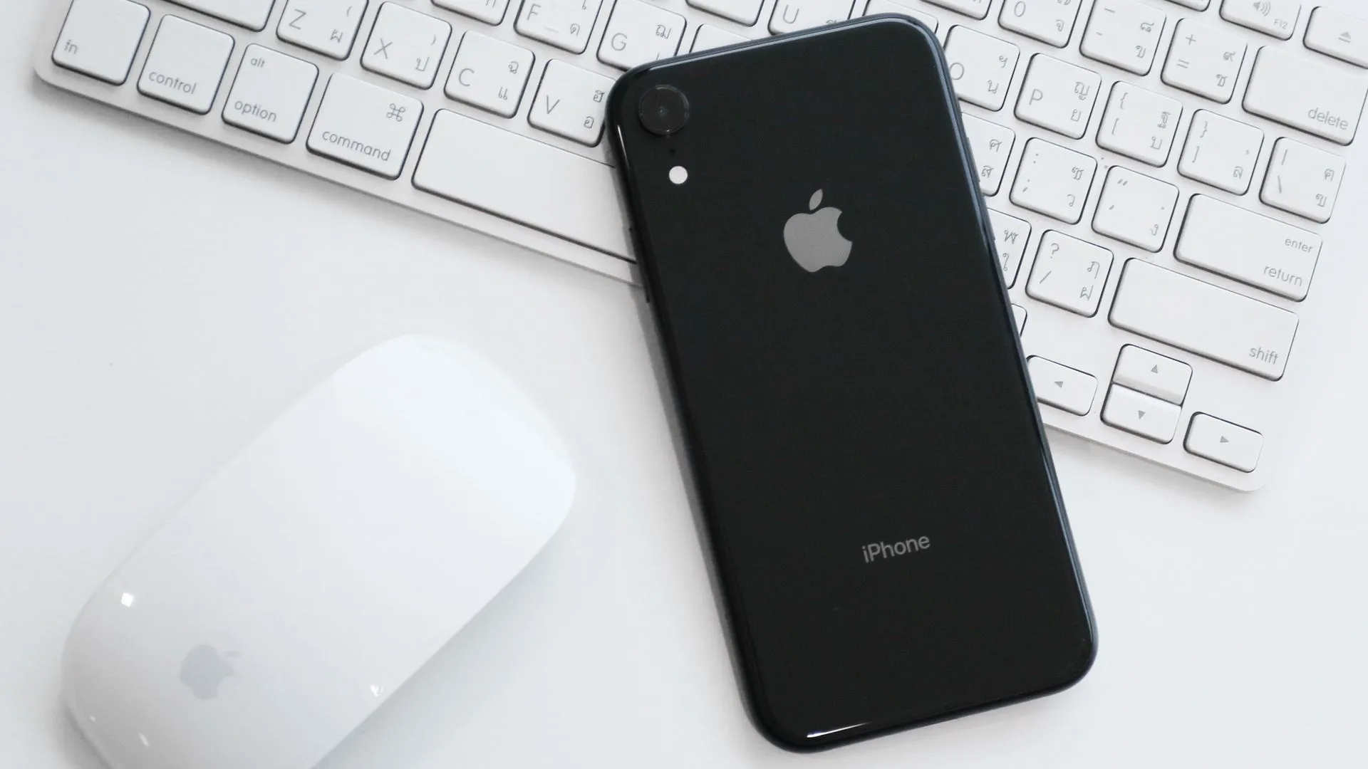 Điện thoại iPhone XR màu trắng đặt trên bàn cùng Magic Mouse và Magic Keyboard, đại diện cho camera đơn chất lượng cao.