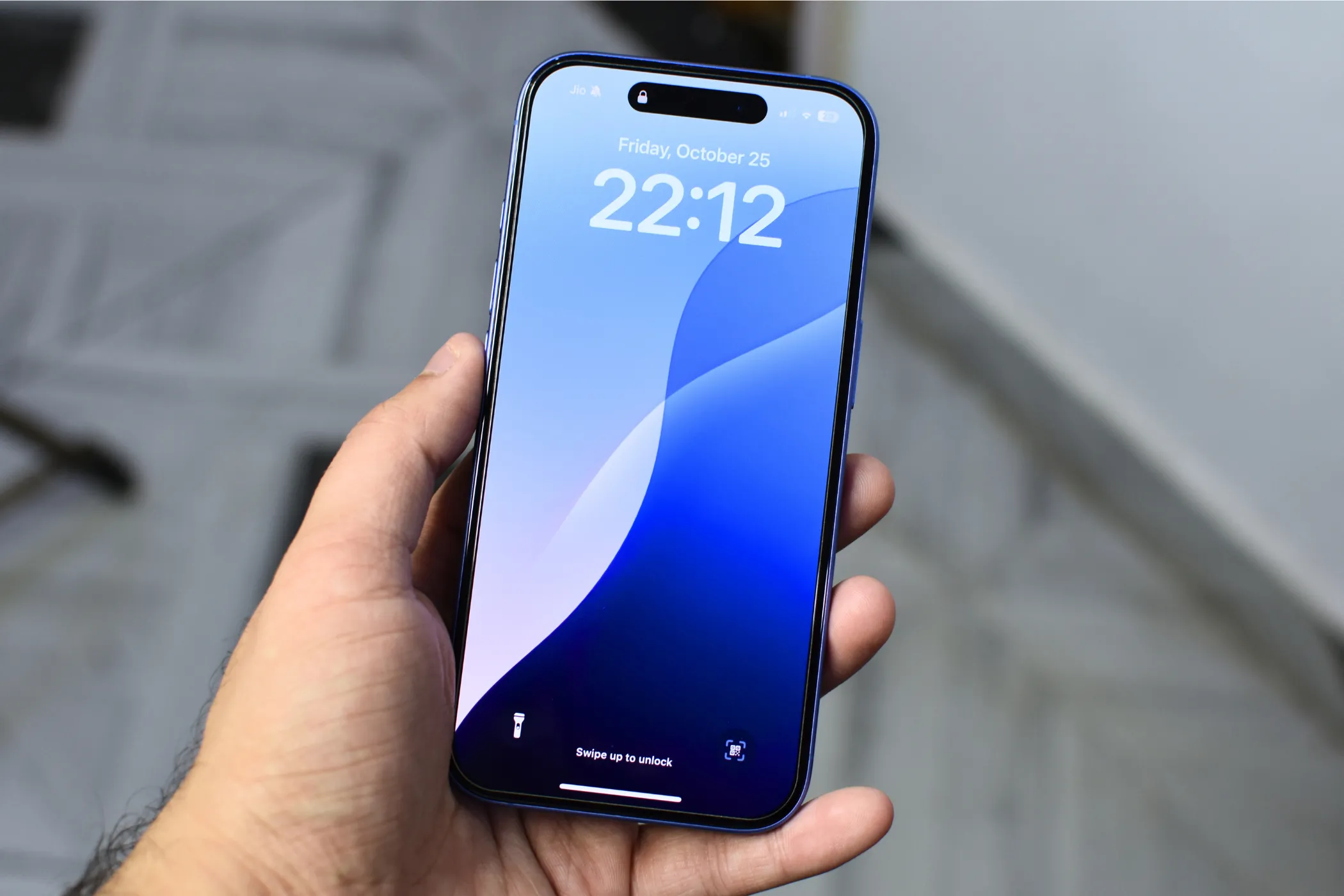 iPhone 16 Plus được cầm trên tay, hiển thị màn hình Super Retina XDR với hình nền khóa màu xanh.