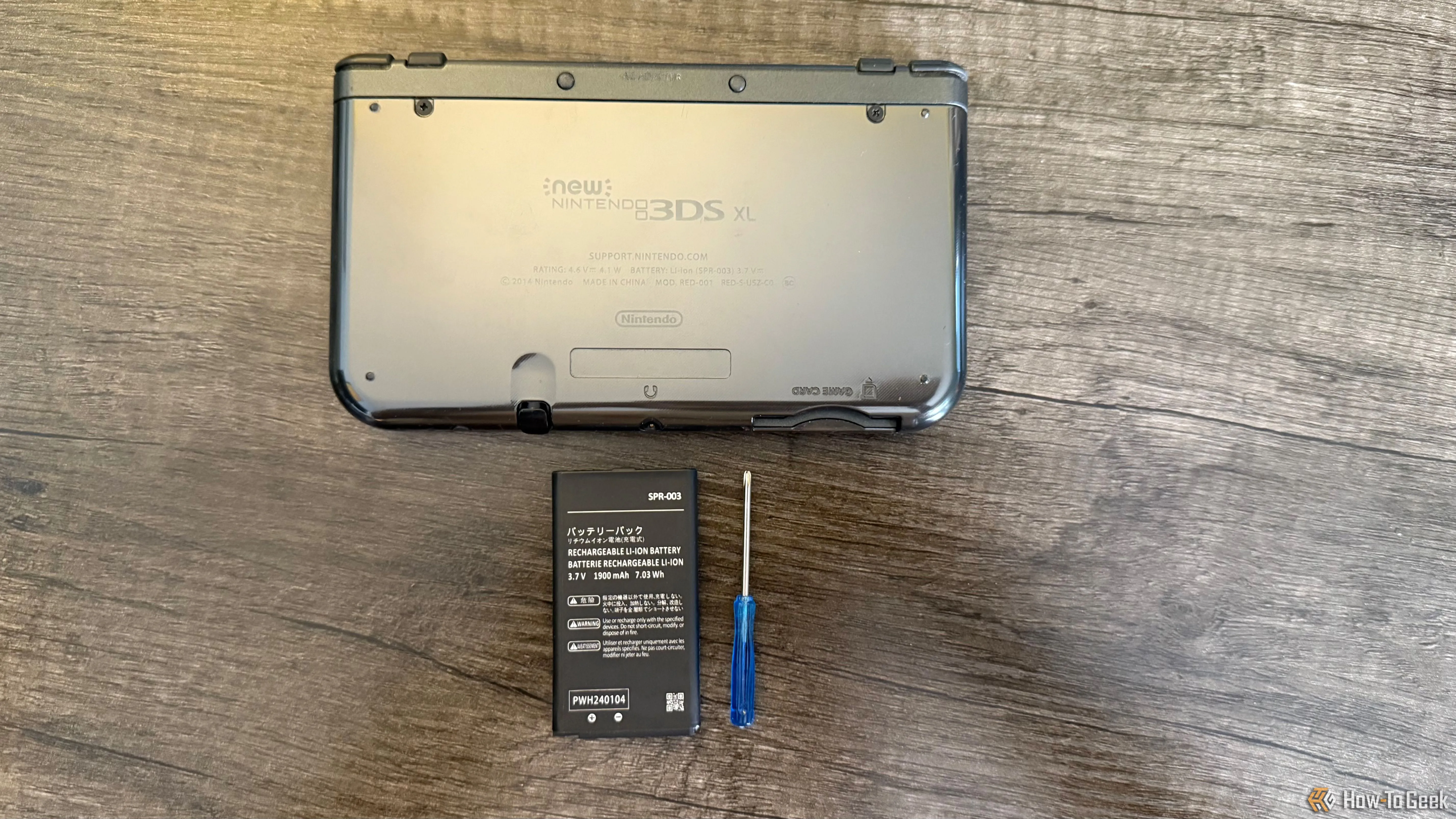 Mặt sau của New Nintendo 3DS XL, kèm pin thay thế và tuốc nơ vít Phillips nhỏ gọn, sẵn sàng cho quá trình tháo lắp pin.