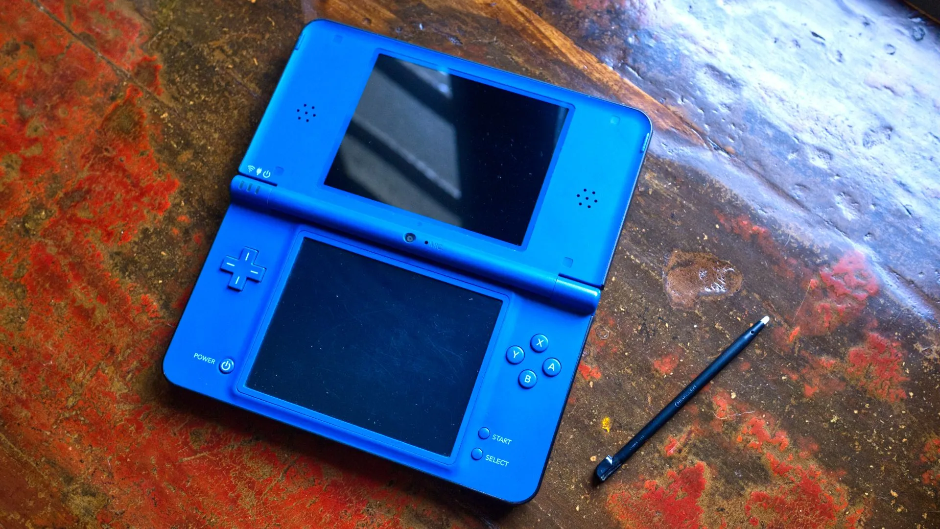 Máy chơi game Nintendo DSi XL màu xanh dương mở ra cùng bút stylus, ví dụ về các handheld cổ điển có màn hình nhỏ.