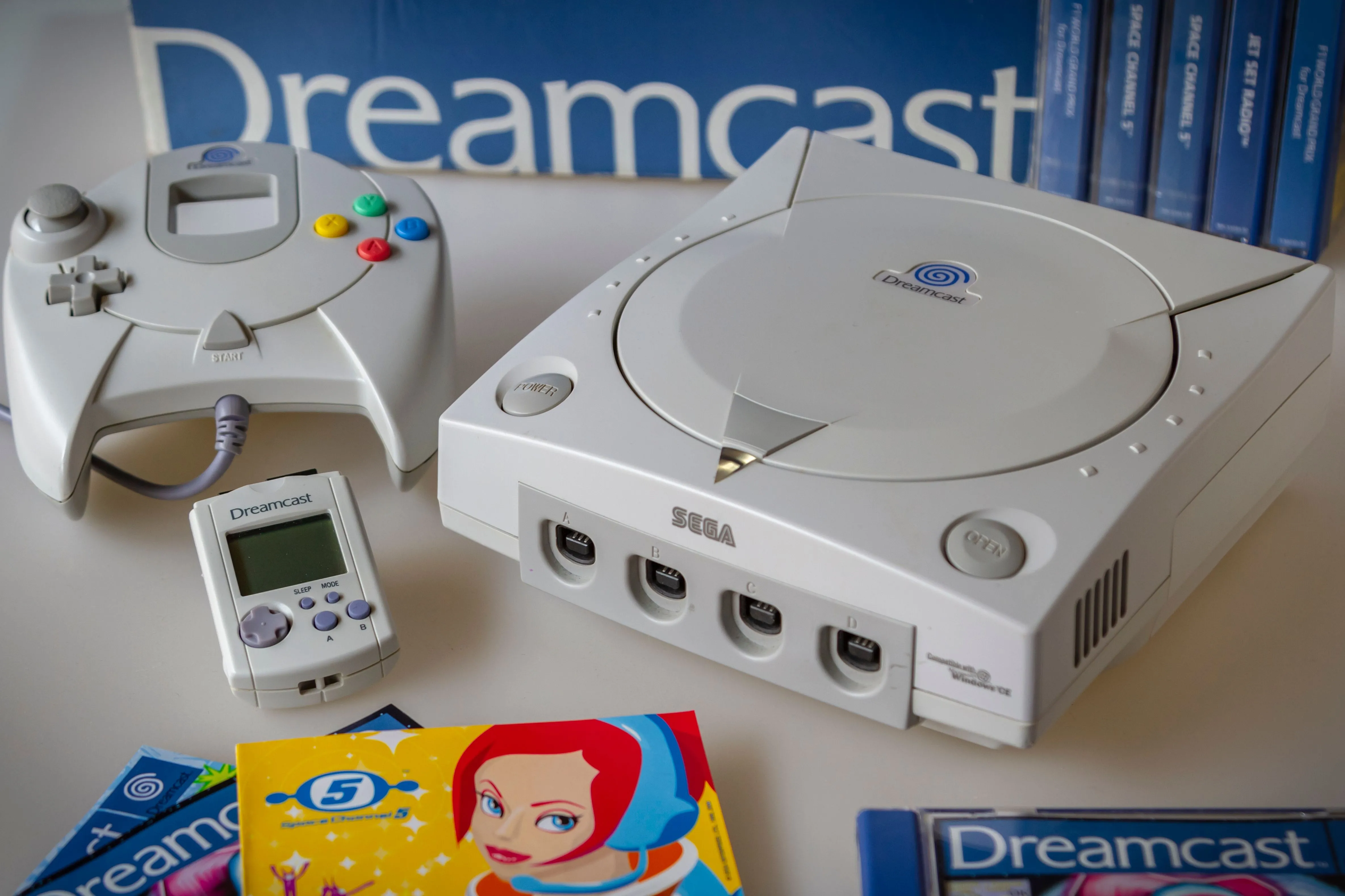 Máy chơi game Sega Dreamcast màu trắng với bộ điều khiển, VMU và đĩa game Space Channel 5 trên mặt phẳng gỗ