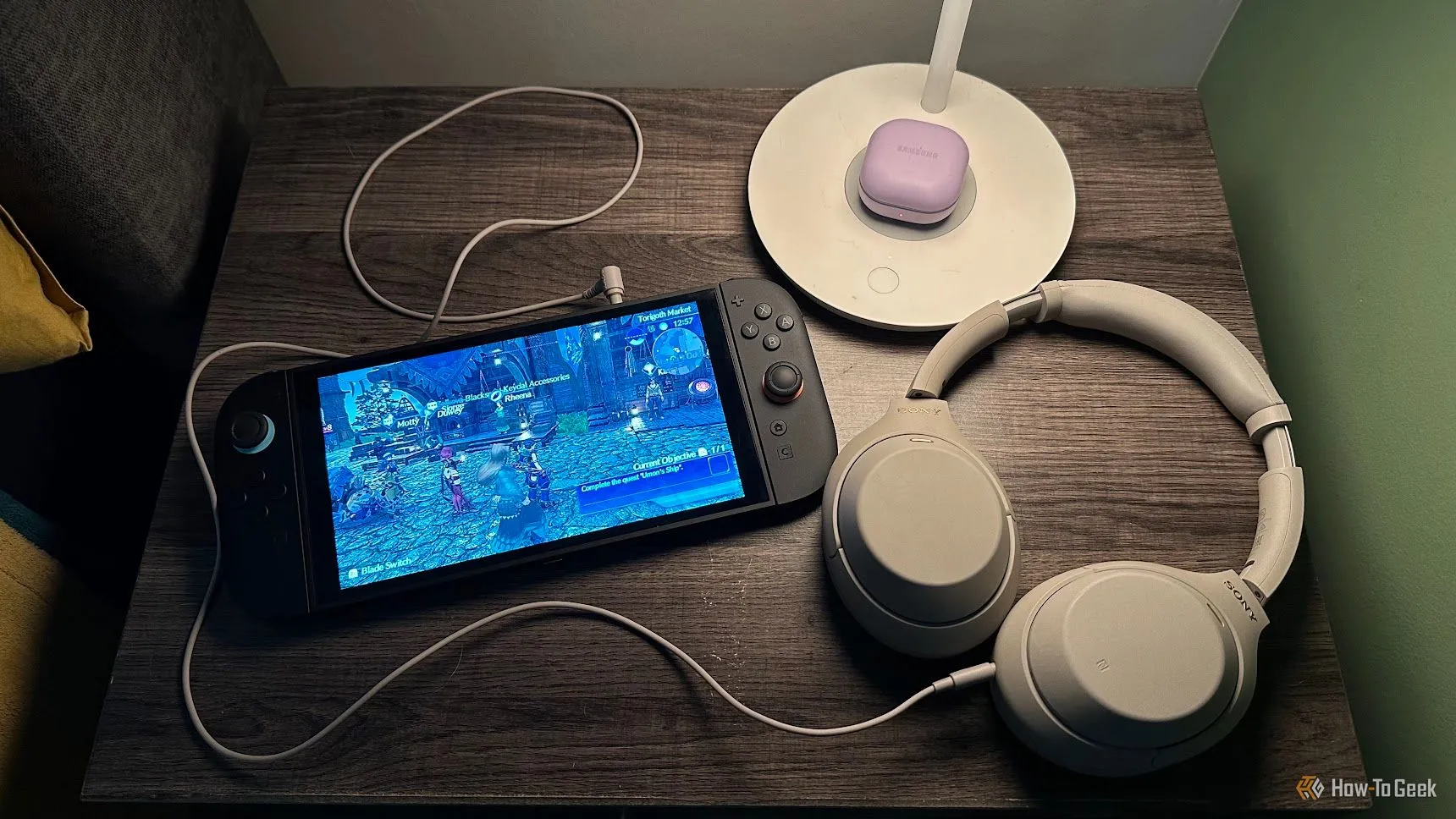 Máy Nintendo Switch 2 và tai nghe Sony WH-1000XM đặt trên bàn cạnh giường, biểu tượng cho việc giải trí công nghệ di động.
