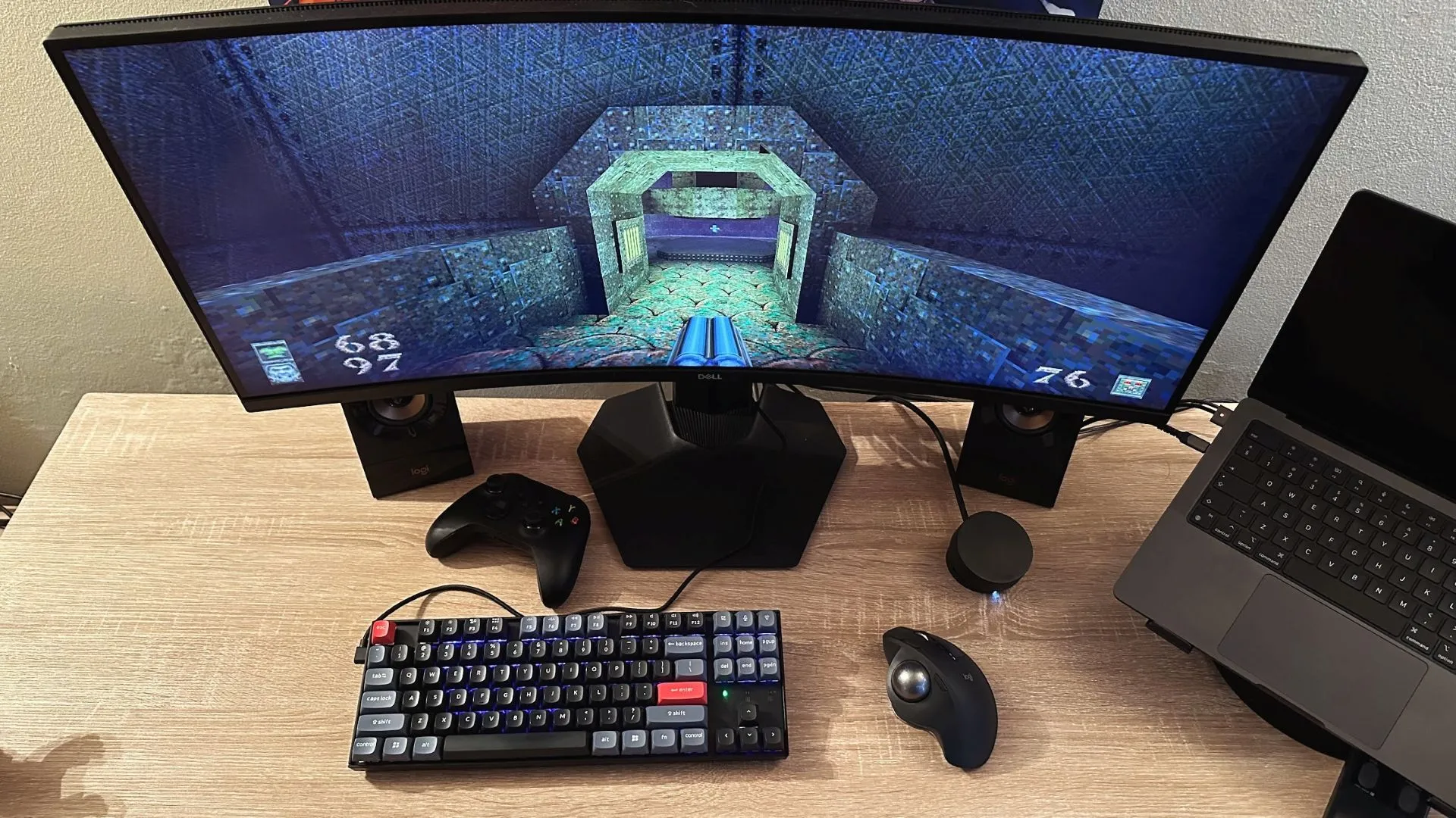 Một bàn làm việc với thiết lập chơi game, hiển thị game Quake trên màn hình máy tính, cùng với một con chuột bi lăn cổ điển trên bàn.