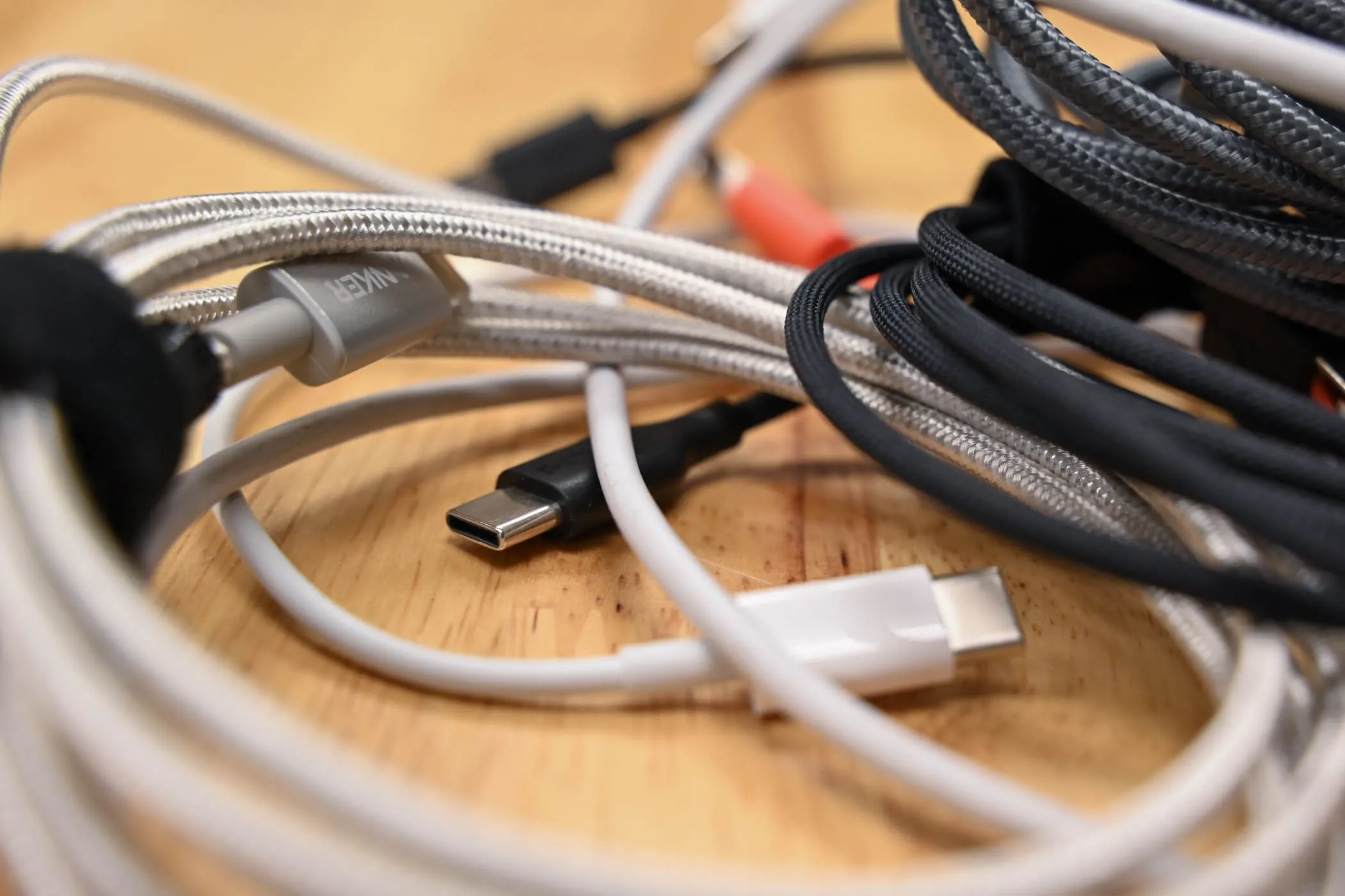 Một chồng cáp sạc USB-C các loại trên bề mặt gỗ, nhấn mạnh sự đa dạng và cần thiết của cáp sạc.