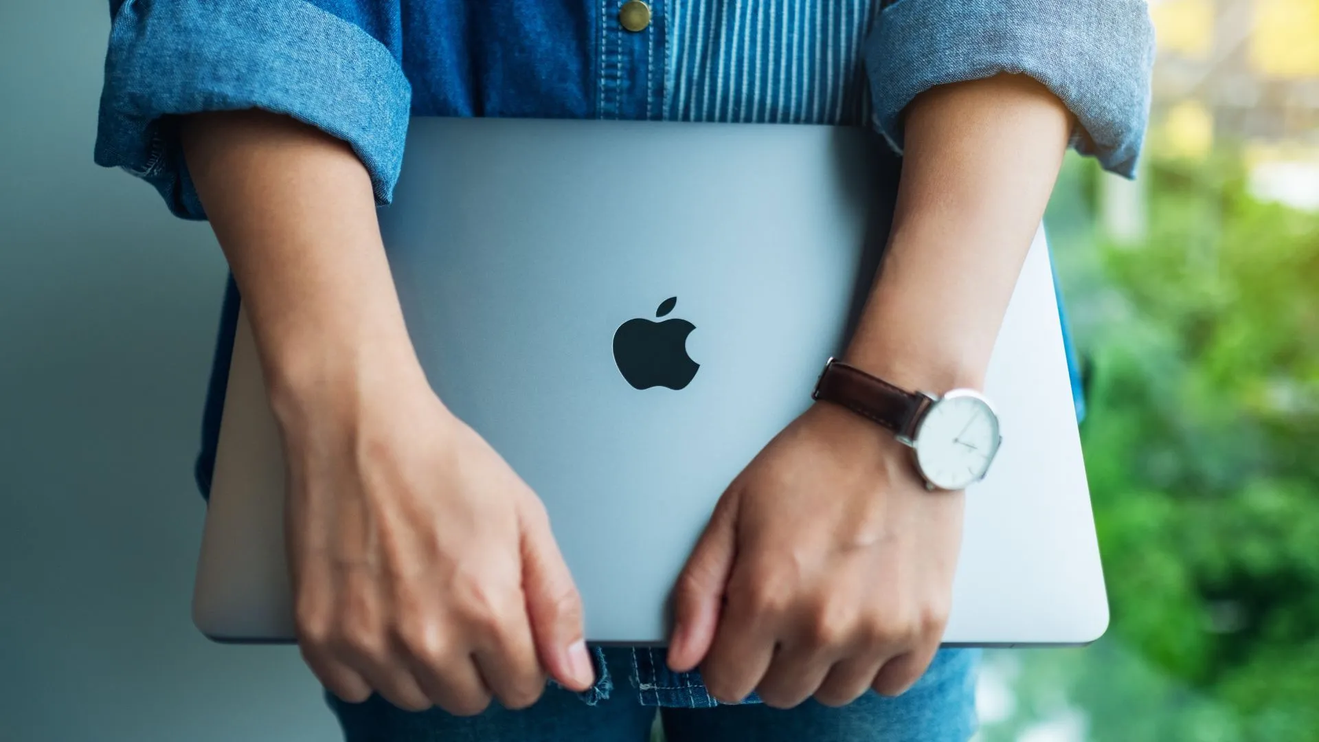Một phụ nữ đang cầm máy tính xách tay Apple MacBook Pro, thể hiện chiến lược thương hiệu cao cấp và giá sửa chữa đắt đỏ của Apple