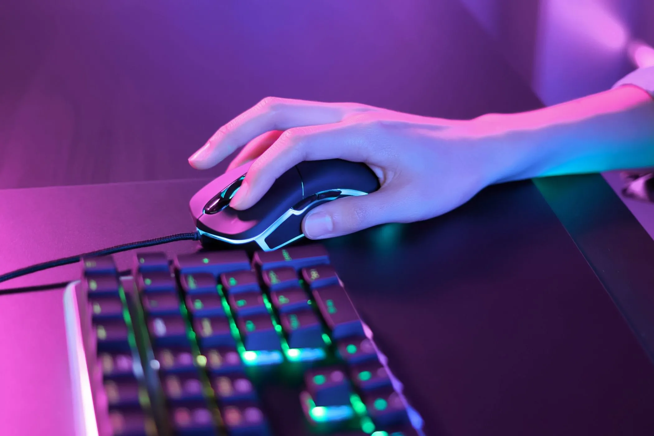 Người chơi sử dụng chuột gaming dưới ánh đèn neon hồng cạnh bàn phím RGB