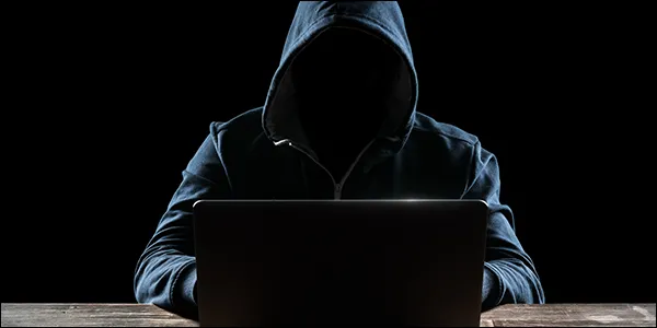 Người đàn ông mặc áo hoodie đang hack vào máy tính xách tay trong bóng tối, biểu tượng cho hoạt động tội phạm mạng.