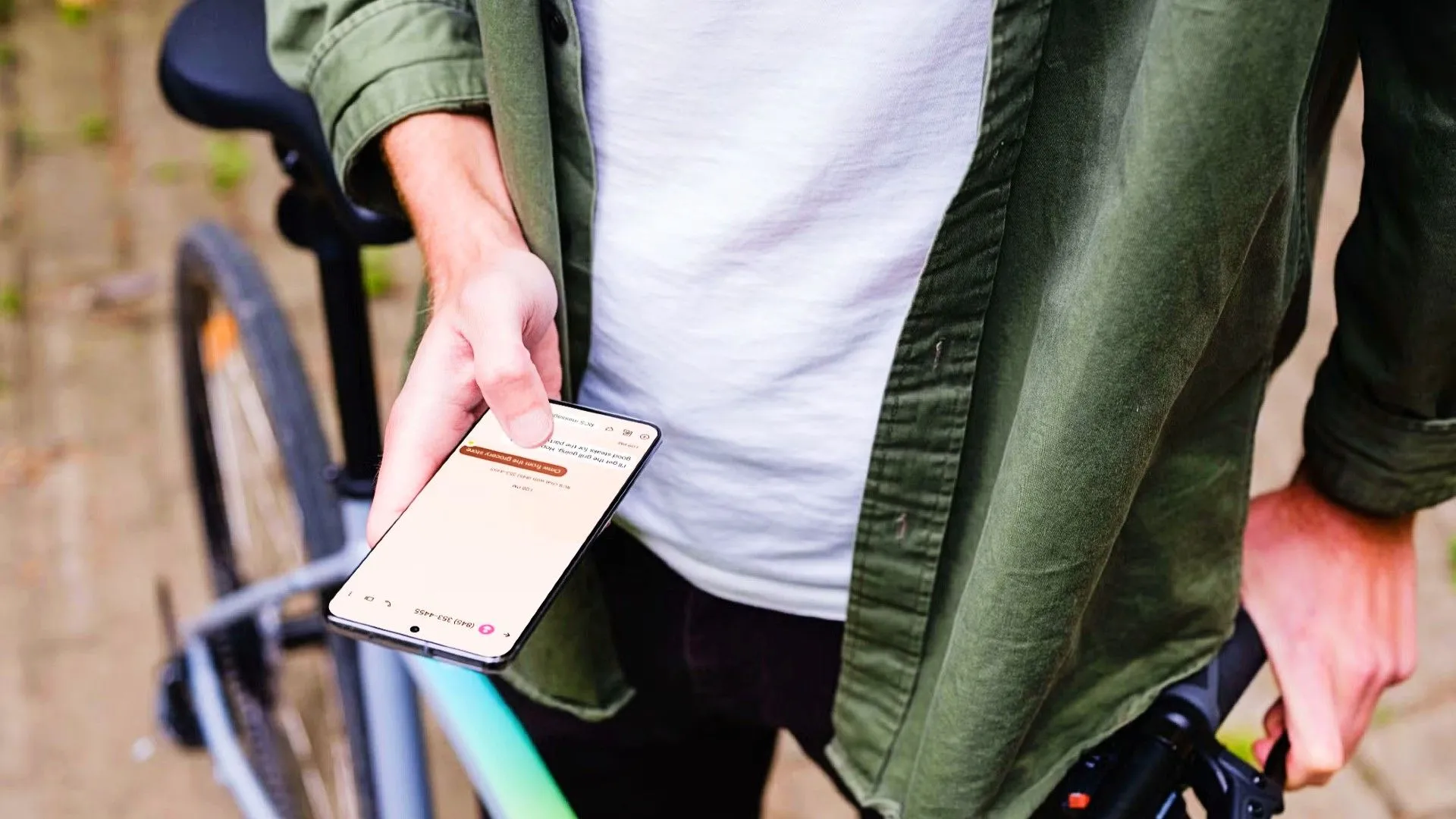 Người đang đứng cạnh xe đạp và cầm thiết bị Android của mình, trên điện thoại có một cuộc trò chuyện tin nhắn
