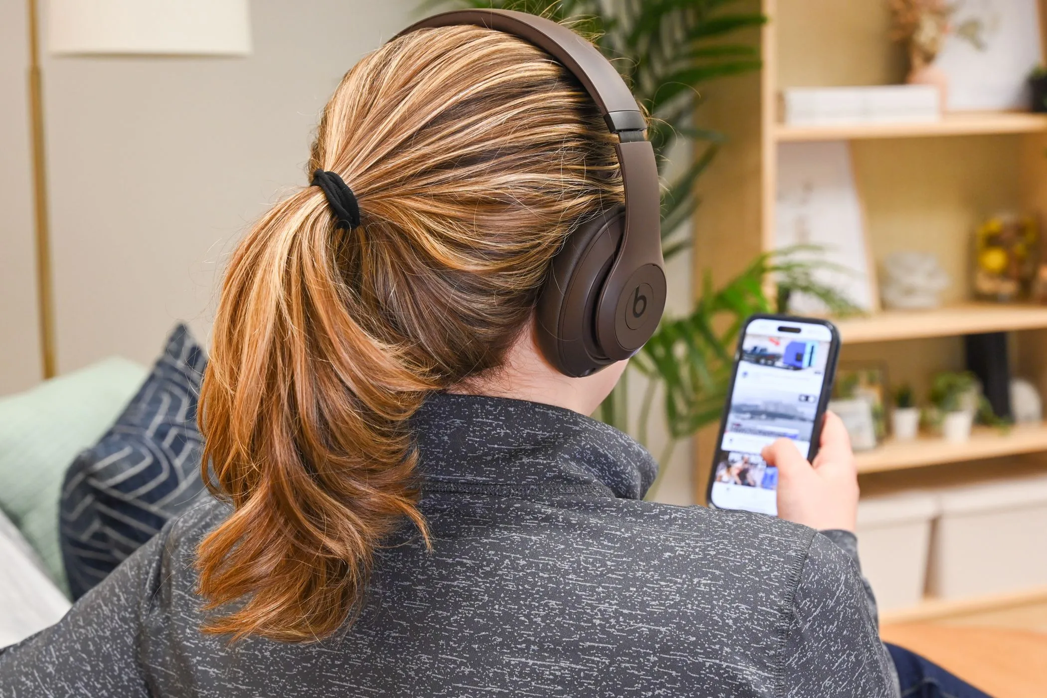 Người dùng đeo tai nghe Beats Studio Pro xem video trên iPhone, tượng trưng cho việc tiêu thụ nội dung được cá nhân hóa trong buồng vang thuật toán.