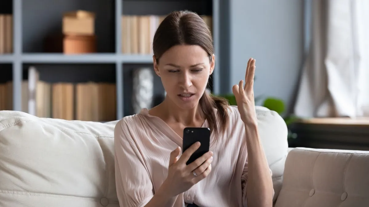 Người phụ nữ nhìn điện thoại với vẻ bối rối hoặc thất vọng, minh họa phản ứng tiêu cực trước nội dung trên mạng xã hội.