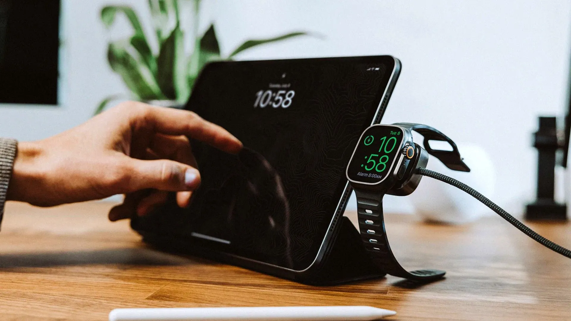 Cáp sạc đa năng Nomad dành cho Apple Watch đang được sử dụng trên bàn cạnh máy tính bảng, thể hiện sự tiện lợi của giải pháp sạc tất cả trong một.