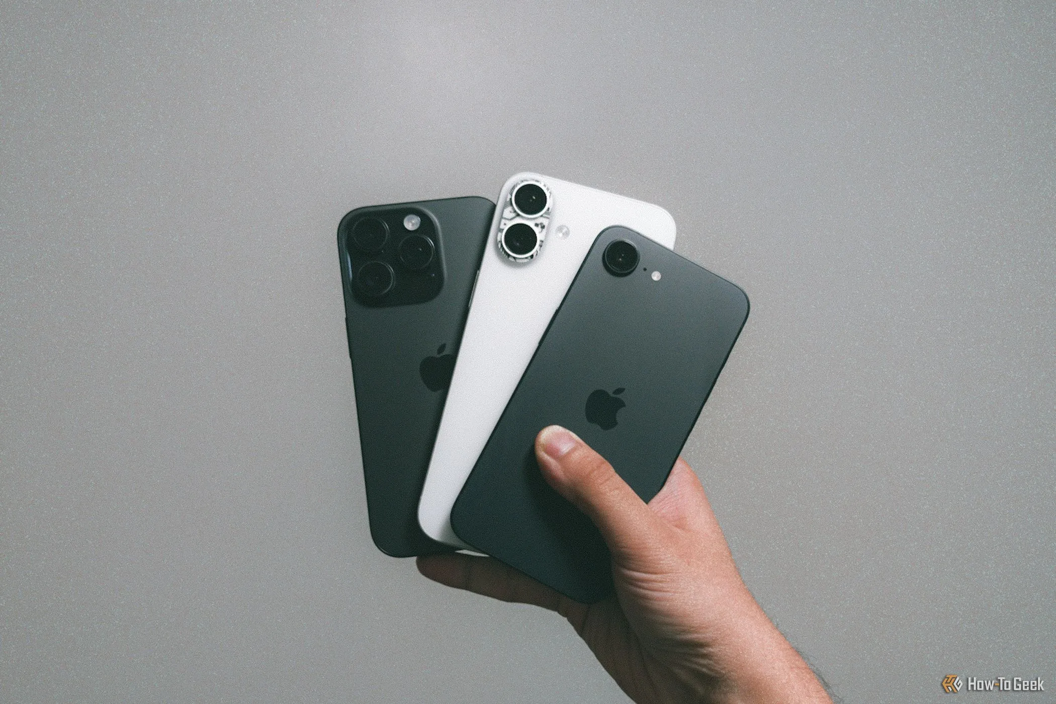 Ba mẫu iPhone 16 khác nhau được cầm trên tay trước bức tường xám, thể hiện sự tương đồng về thiết kế