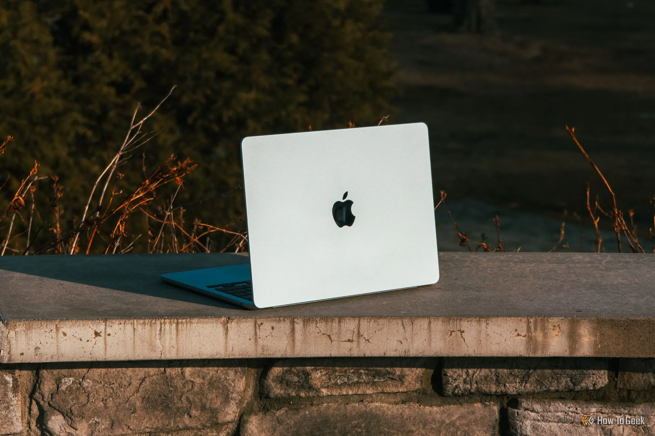 MacBook Air M4 màu xanh da trời đặt nghiêng trên một gờ bê tông dưới ánh nắng mặt trời