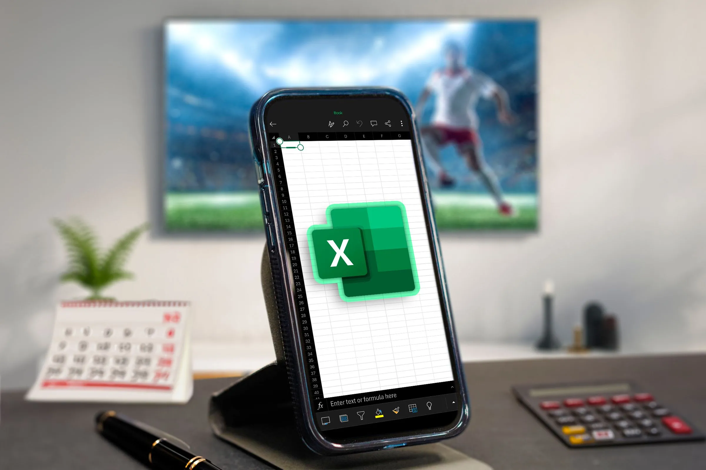 Một chiếc điện thoại đang mở Excel, một số vật dụng văn phòng xung quanh và TV ở phía sau